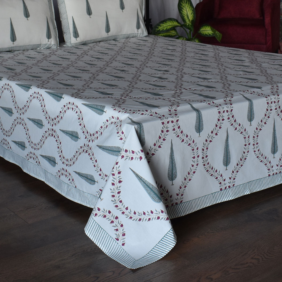 A white bedspread with a repeating gray geometric lattice pattern and muted green teardrop motifs, draped over a bed with matching pillows in a bedroom setting.