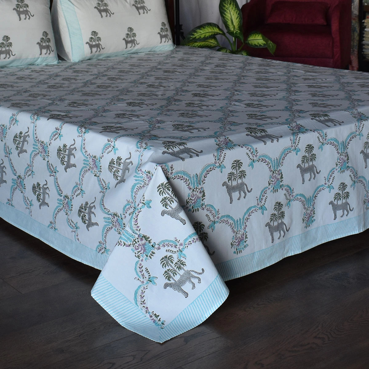 A light blue and white cotton bedspread with a repeating palm tree and elephant block print pattern, styled on a bed with matching pillows in a bedroom setting.