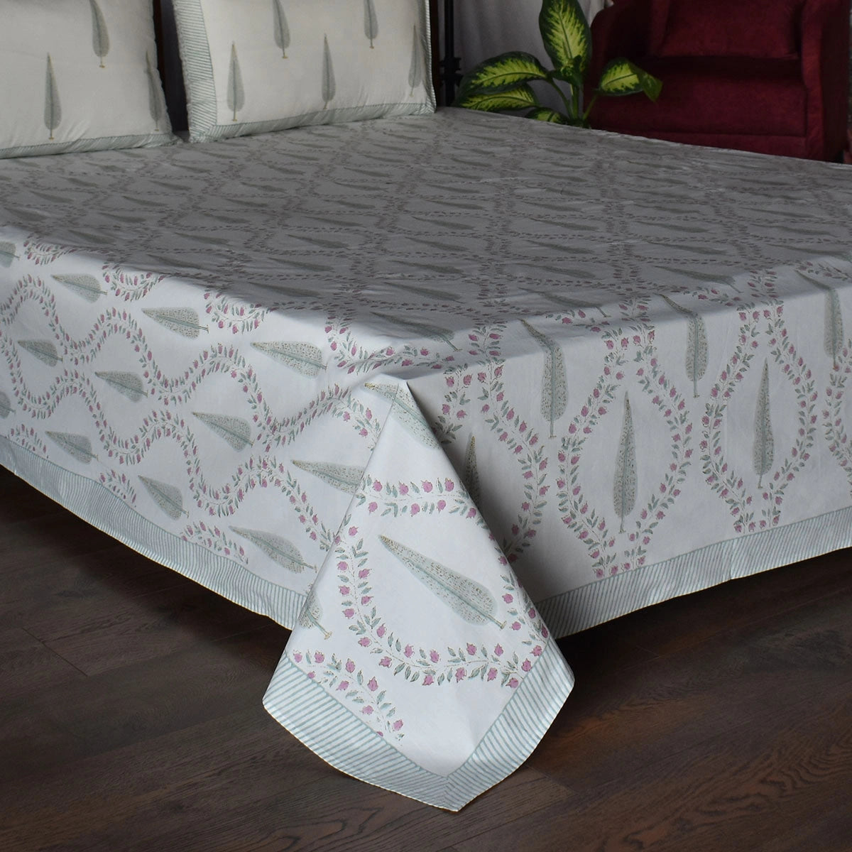 A white bedspread with a gray geometric lattice pattern and pink floral accents, styled on a bed with matching pillows in a bedroom setting.