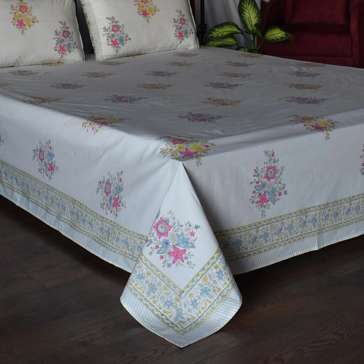 A white tablecloth with a colorful floral pattern and a decorative border, draped over a bed in a bedroom setting.