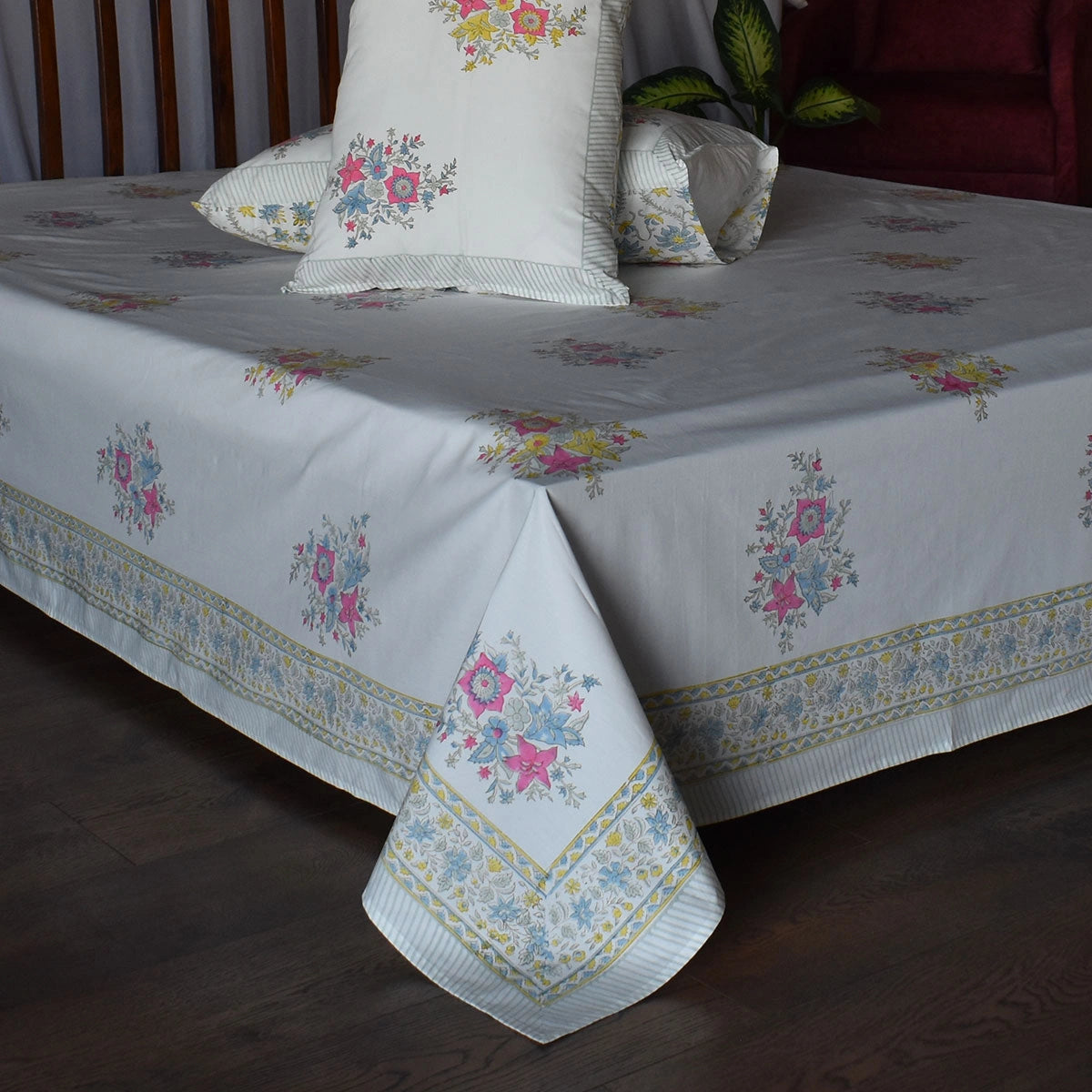 A white bedspread and matching pillow shams decorated with a pastel floral pattern and a decorative border, styled on a bed in a bedroom setting.