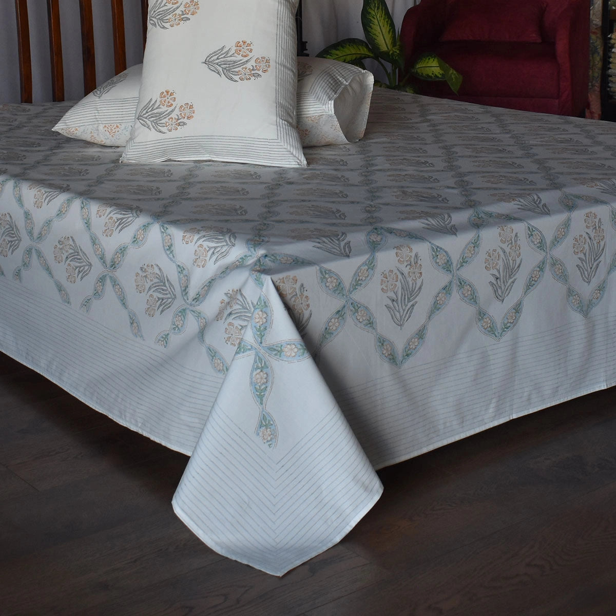 A white bedspread with a light blue and beige floral pattern, styled on a bed with matching pillows in a bedroom setting.