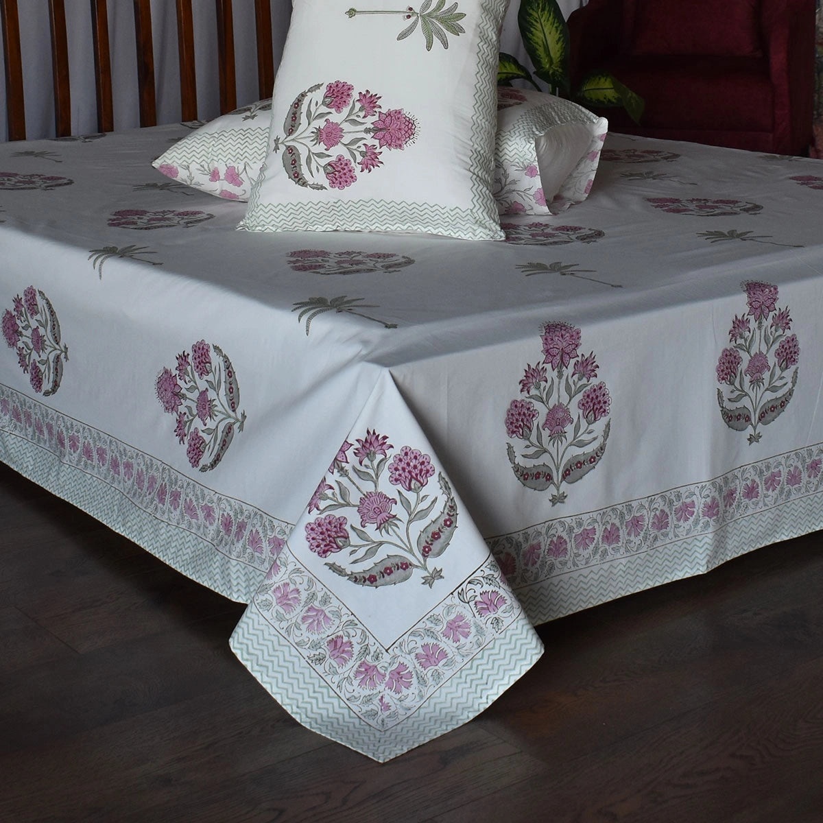 A white cotton bed sheet with pink and gray floral block prints and a decorative border, shown on a bed with matching pillowcases in a bedroom setting.