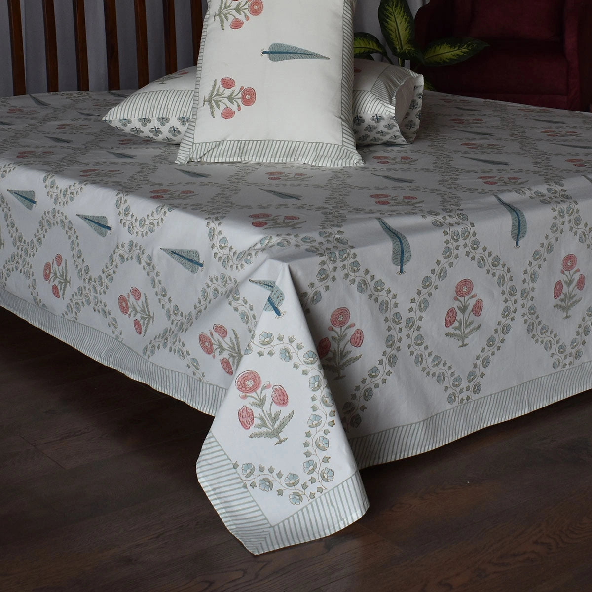 A white cotton bed sheet set with a delicate floral and leaf pattern in muted pink and sage green, styled on a bed with matching pillowcases.