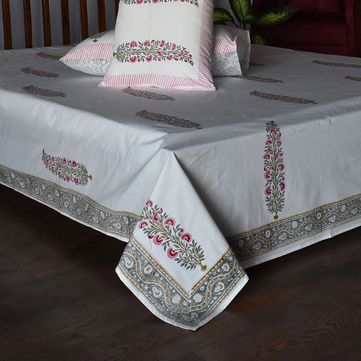 A white cotton bed sheet with pink and green floral block prints and a decorative border, styled on a bed with matching pillows in a bedroom setting.
