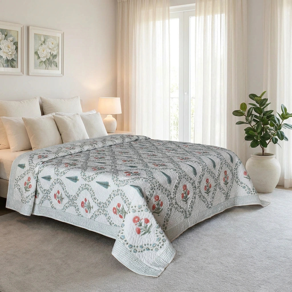 A patterned quilted comforter set on a bed in a bright, modern bedroom. The comforter features a white base with a gray geometric lattice pattern and small red and green floral accents.