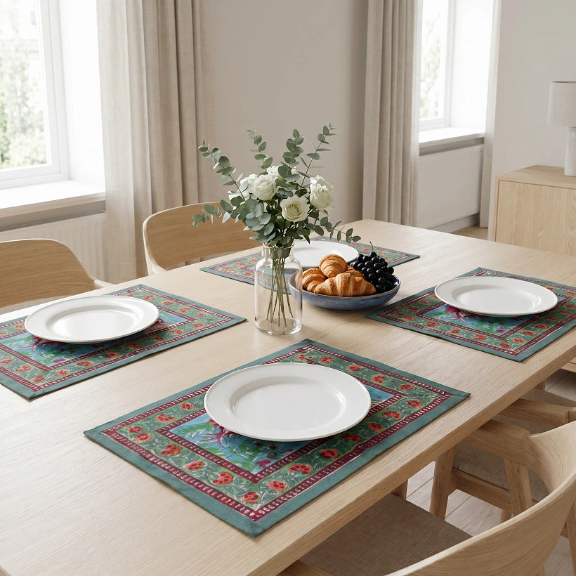 Four rectangular table placemats with a teal and red traditional pattern are arranged on a light wood dining table, each styled with a white plate, in a bright, modern dining room.