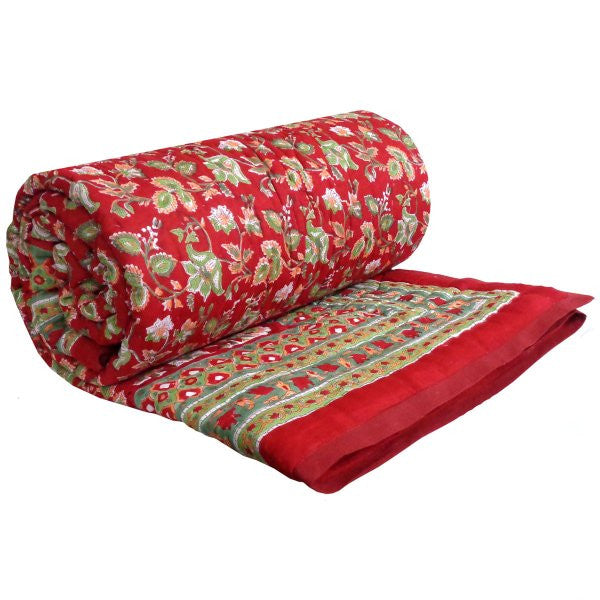 A folded red quilt or comforter with a floral pattern and a decorative border, shown rolled up on a plain white background.