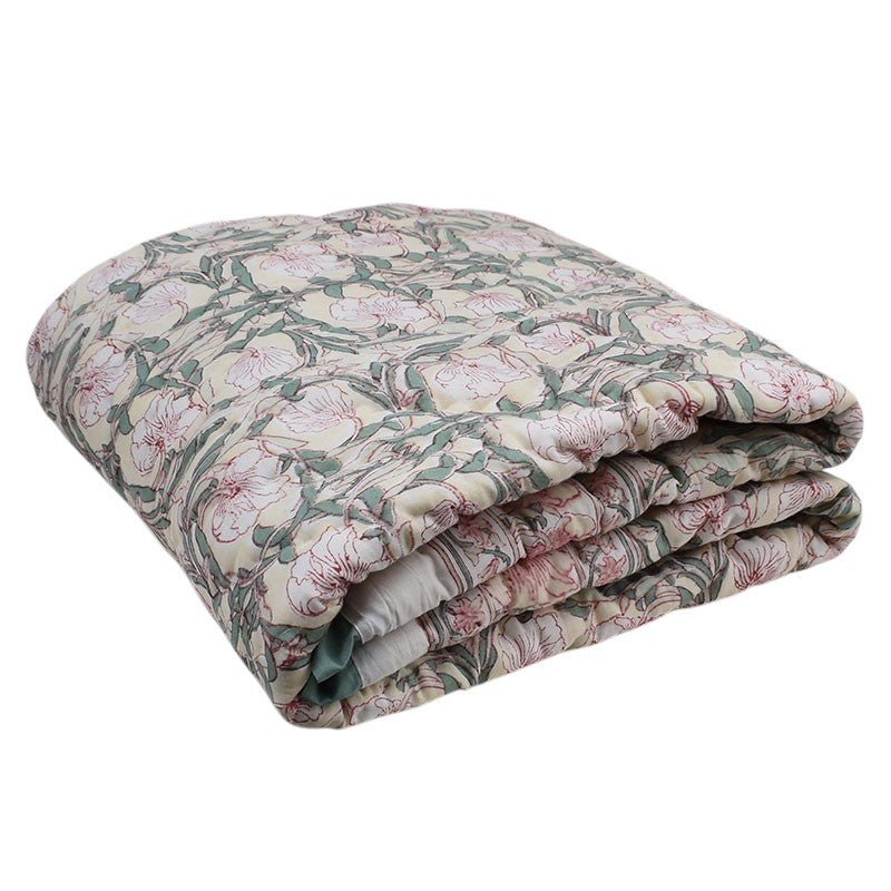 A folded quilted comforter with a vintage floral pattern in muted pink, sage green, and beige tones, isolated on a white background.