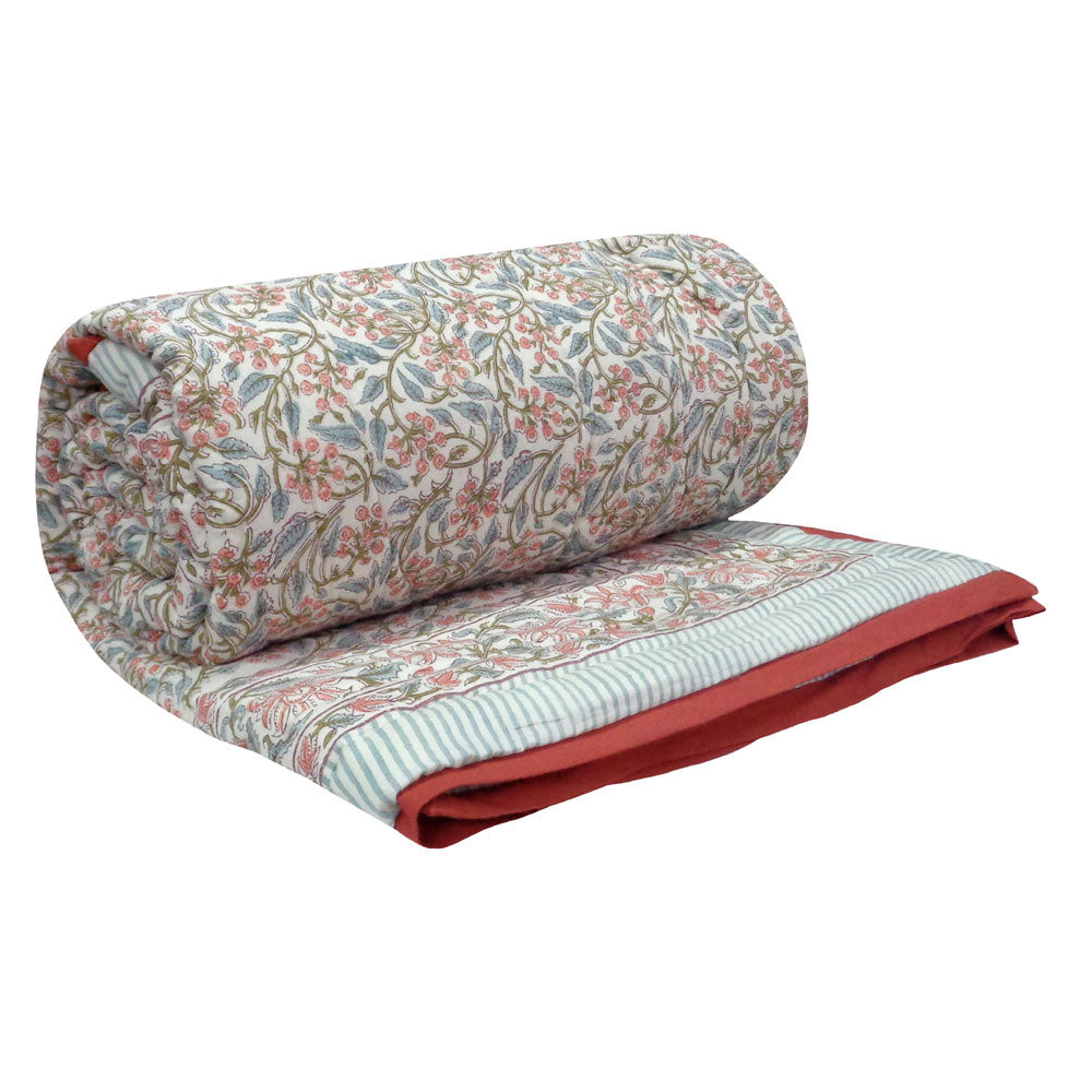 A rolled and folded quilted blanket featuring a vintage floral pattern in muted pink, green, and blue on a cream background, with a striped border and a solid rust-red underside.