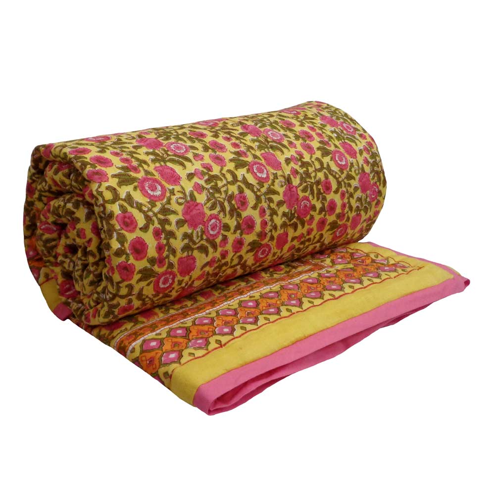 A rolled and partially unrolled block-printed cotton quilt or comforter on a solid white background. The fabric features a yellow base with a pink and green floral pattern, a decorative border with orange and pink motifs, and a solid pink edge.