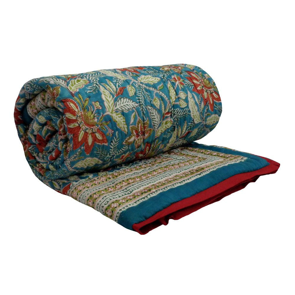 A rolled-out quilted blanket featuring a vibrant floral and botanical pattern in teal blue, red, and cream, with a striped border and solid red edge, shown on a plain white background.