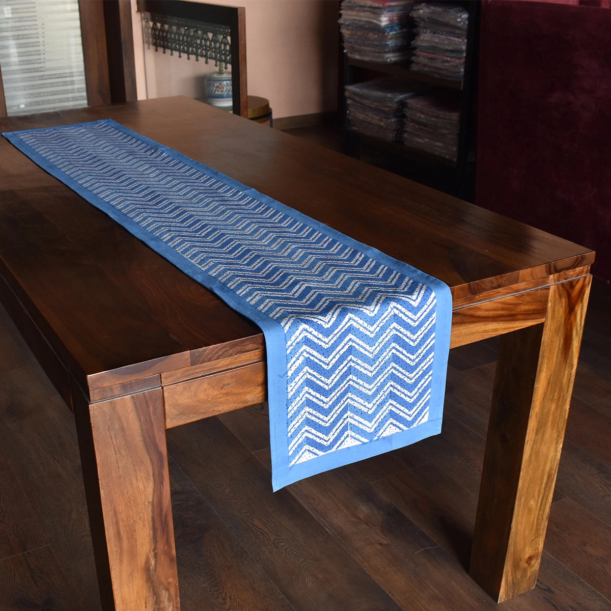 A blue table runner with a white chevron pattern draped over a dark wooden dining table in an indoor room setting.