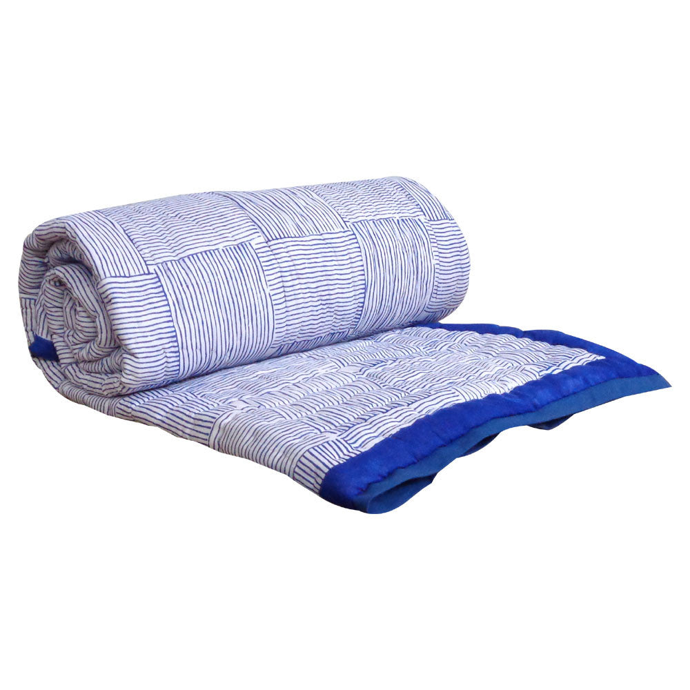 A rolled-out quilted blanket with a blue and white striped pattern and a solid royal blue border, shown on a plain white background.