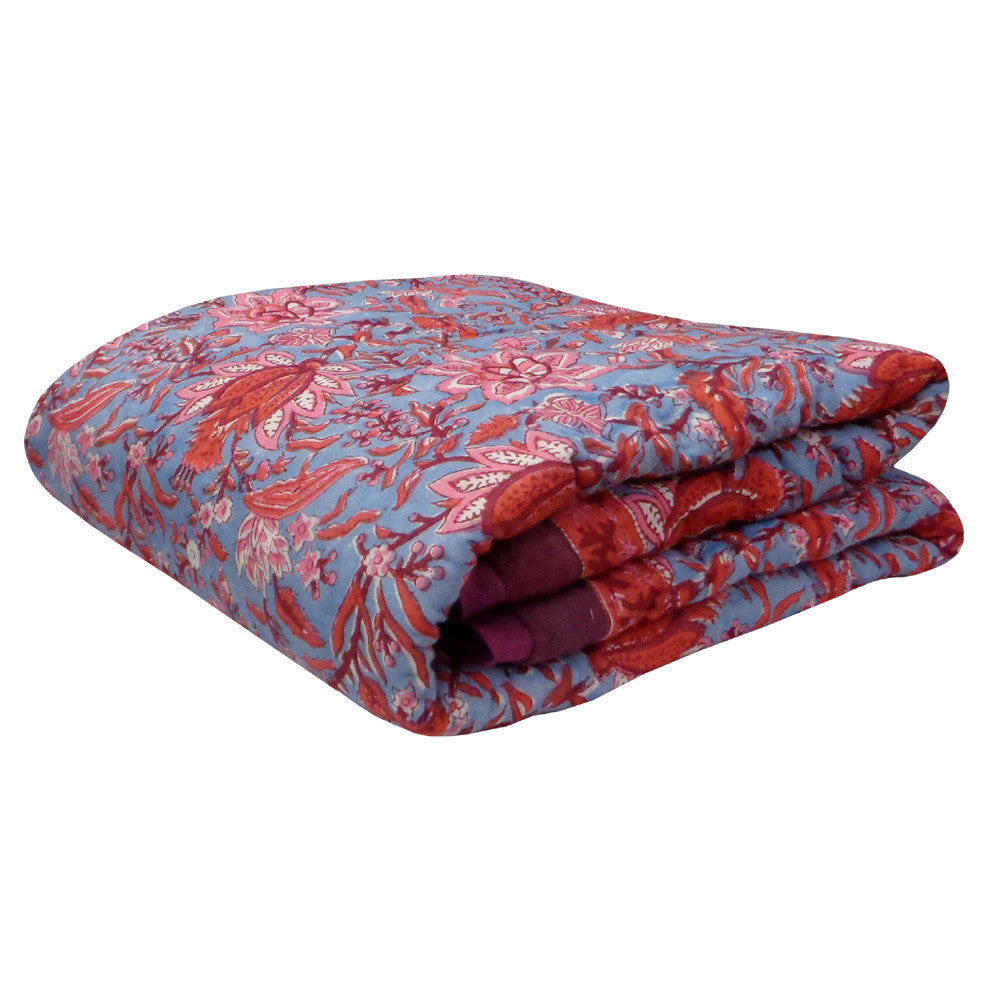 A folded quilted blanket featuring a red and pink paisley pattern on a dusty blue background, with a solid red border.