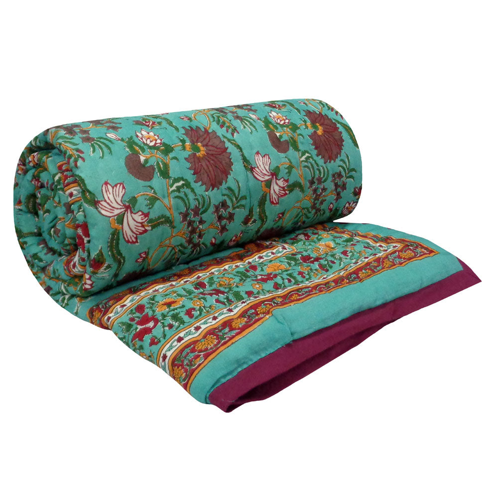 A rolled-out quilted comforter with a vibrant teal background and an intricate floral pattern in red, pink, and green, featuring a decorative border and a solid deep magenta underside.