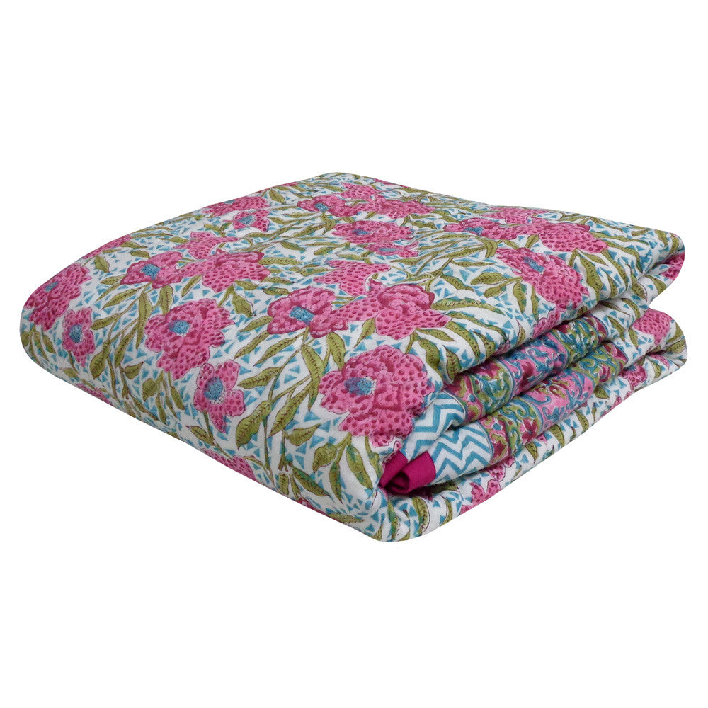 A folded cotton blanket featuring a vibrant pink and green floral block print on a white background, with a small chevron pattern visible on one folded section.