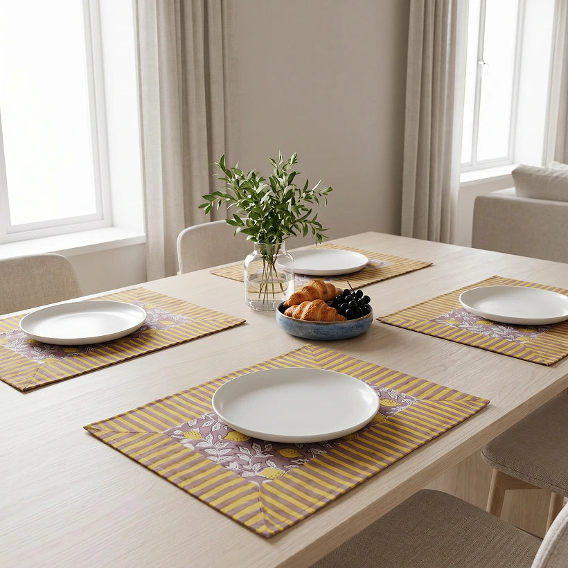 A dining table set with four matching placemats, white plates, and a small vase of greenery in a bright, modern room.