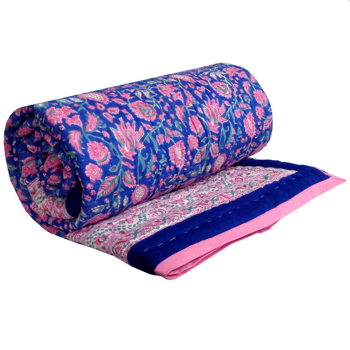 A blue quilted bedspread with pink and white floral and paisley patterns, styled on a bed in a bedroom setting with wooden floors, a red armchair, and decorative pillows.