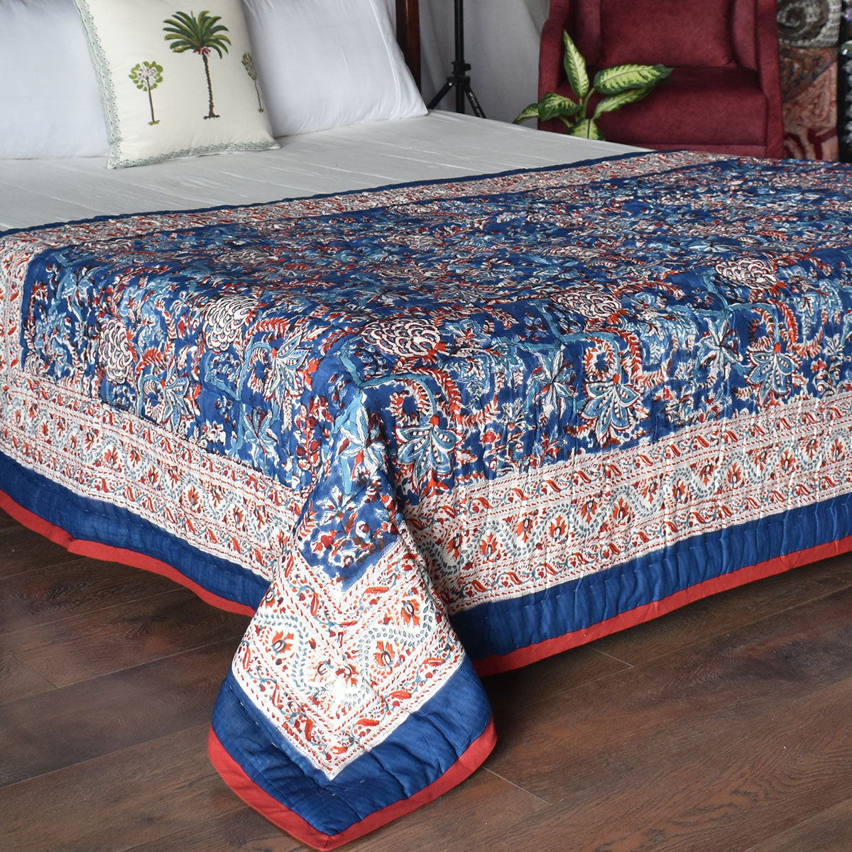A patterned quilted comforter in navy blue, red, and white, styled on a bed with white pillows in a bedroom setting.