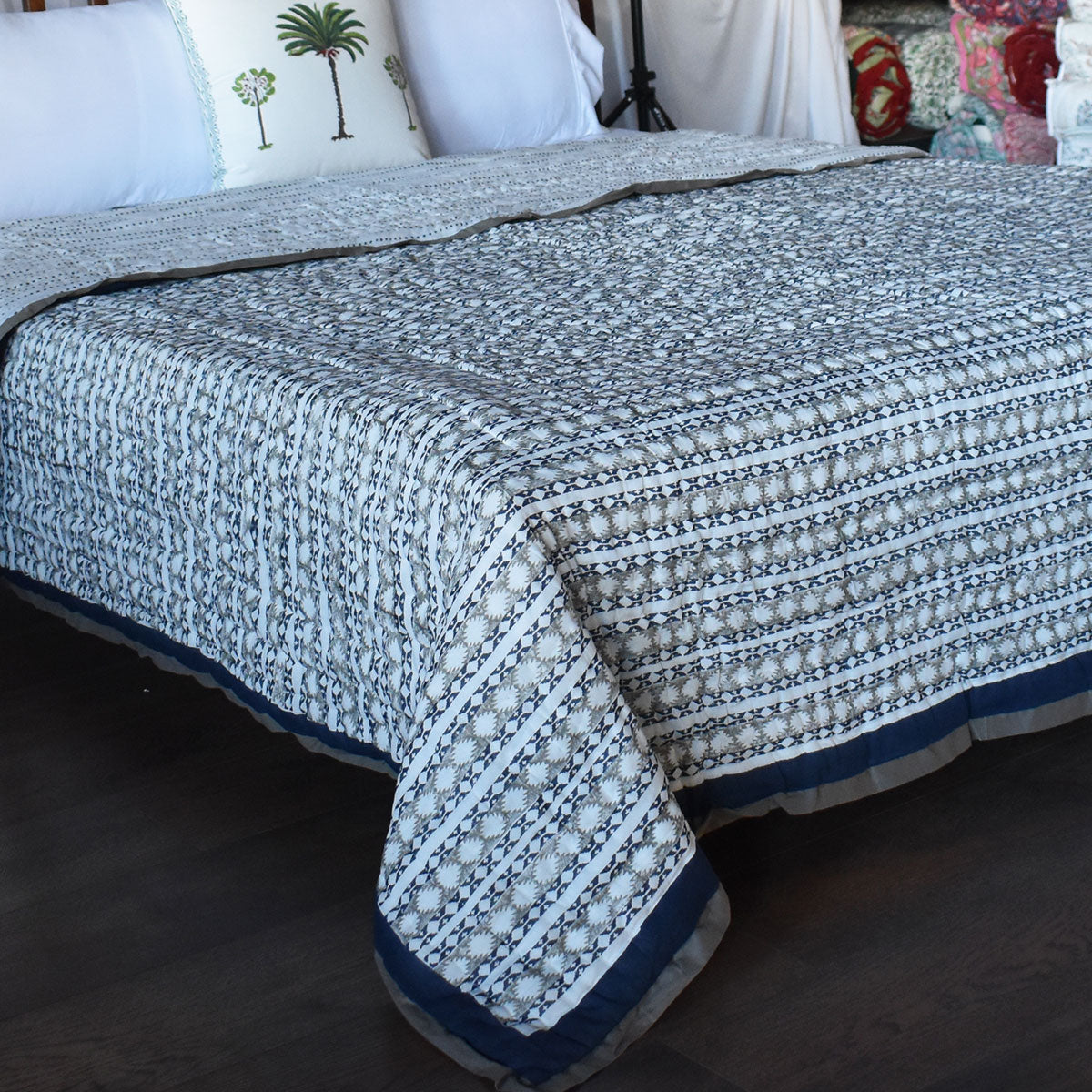 A patterned cotton bedspread with a geometric block print in navy blue and off-white, styled on a bed with white pillows in a bedroom setting.