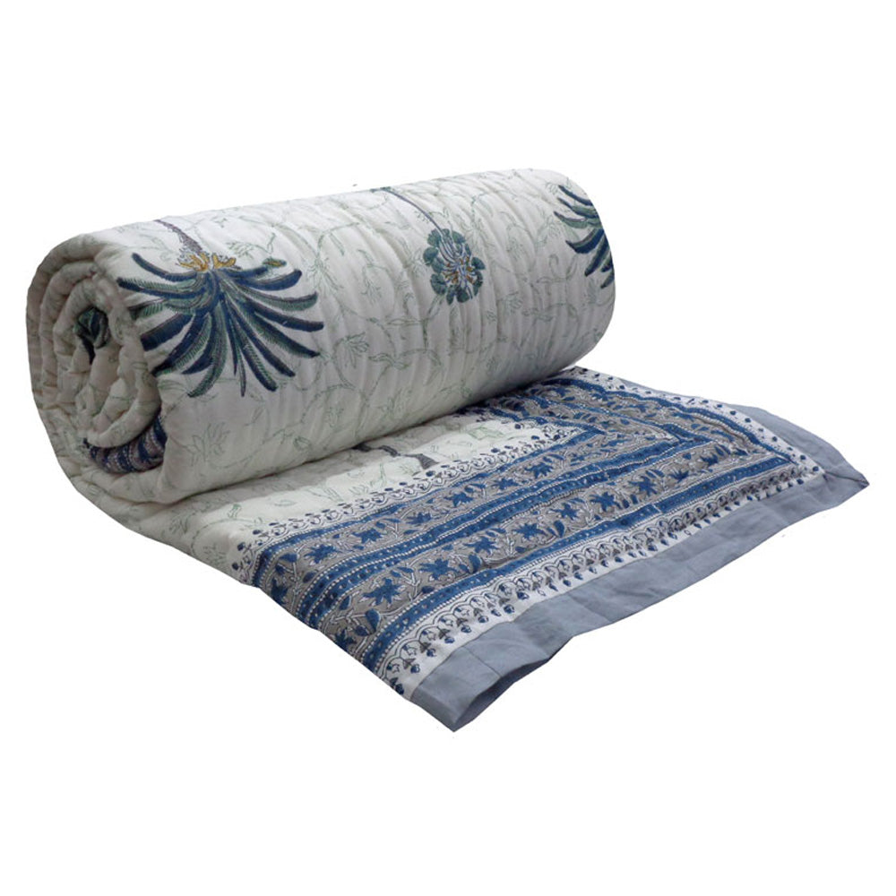 A rolled-up quilted cotton bedspread with blue and gray floral and geometric patterns on a white background, shown against a plain white studio backdrop.