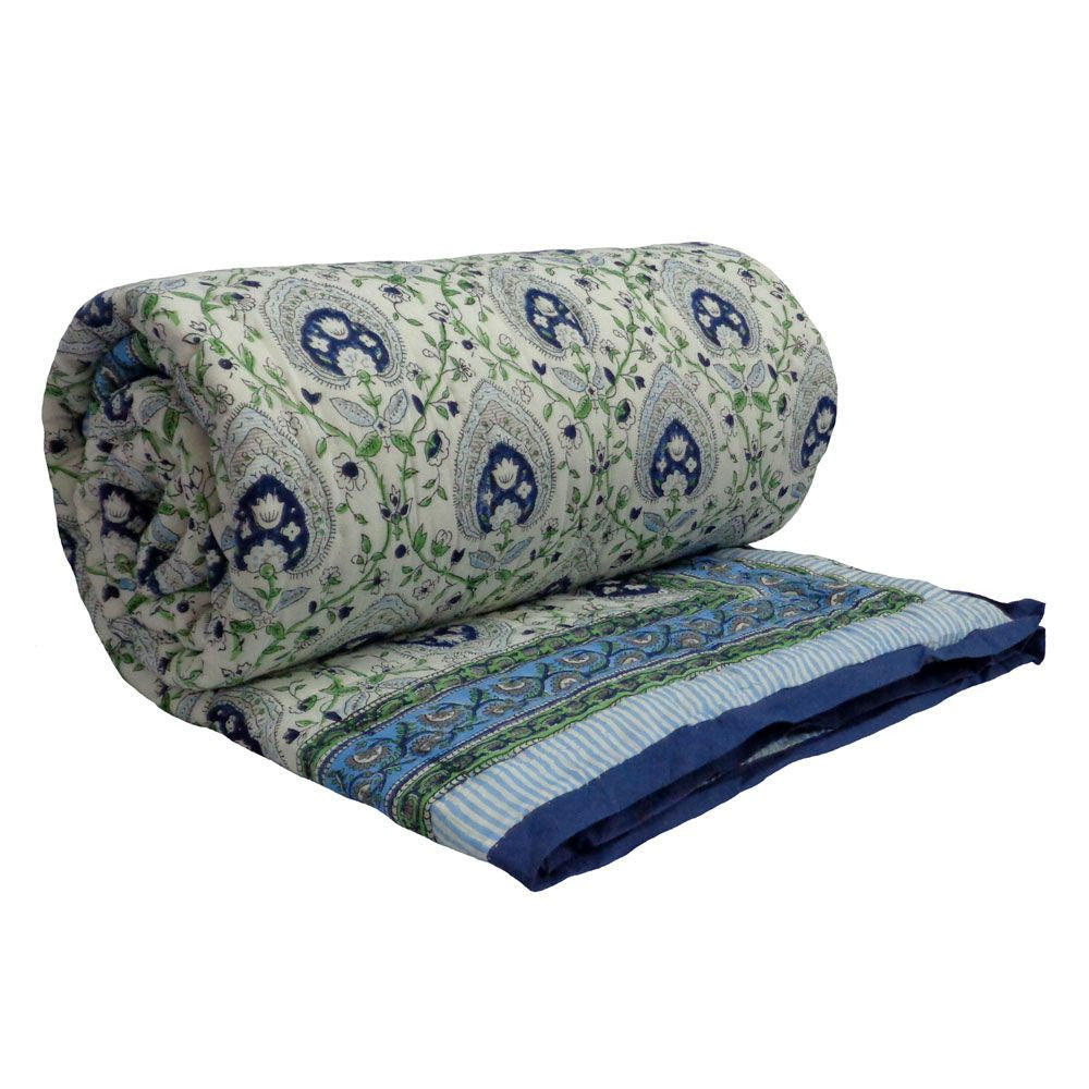 A rolled and partially unrolled quilted blanket featuring a blue and green paisley pattern on a light cream background, with a solid blue striped border.