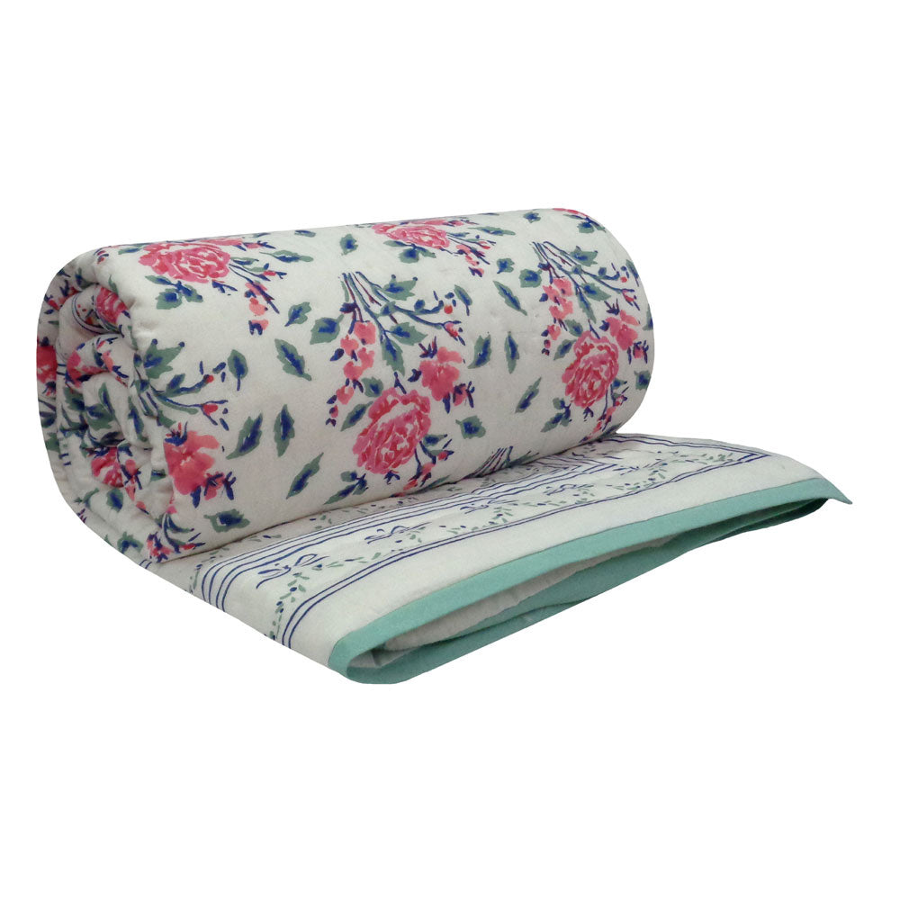A rolled and folded quilted blanket featuring a pink and blue floral pattern on a cream background, with a solid light green border.