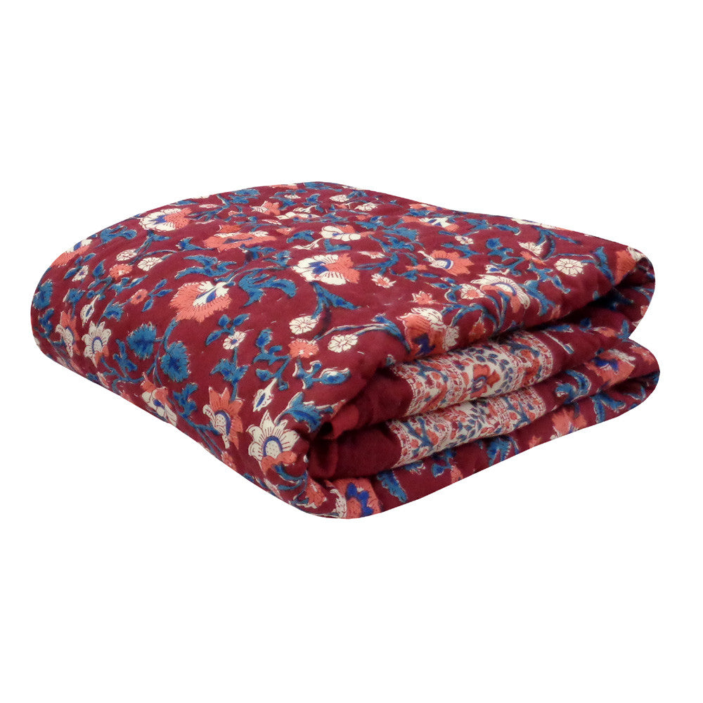 A folded quilted blanket with a red floral pattern, featuring blue, pink, and white flowers, shown on a plain white background.