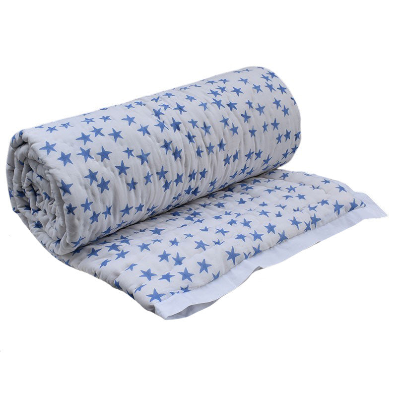 A rolled and flat-laid quilted baby blanket with a blue star pattern on a white background, shown against a plain white studio backdrop.