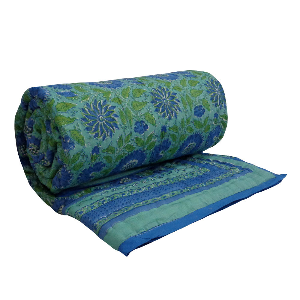 A rolled and partially unrolled quilted fabric piece with a blue and green floral pattern, shown on a plain white background.