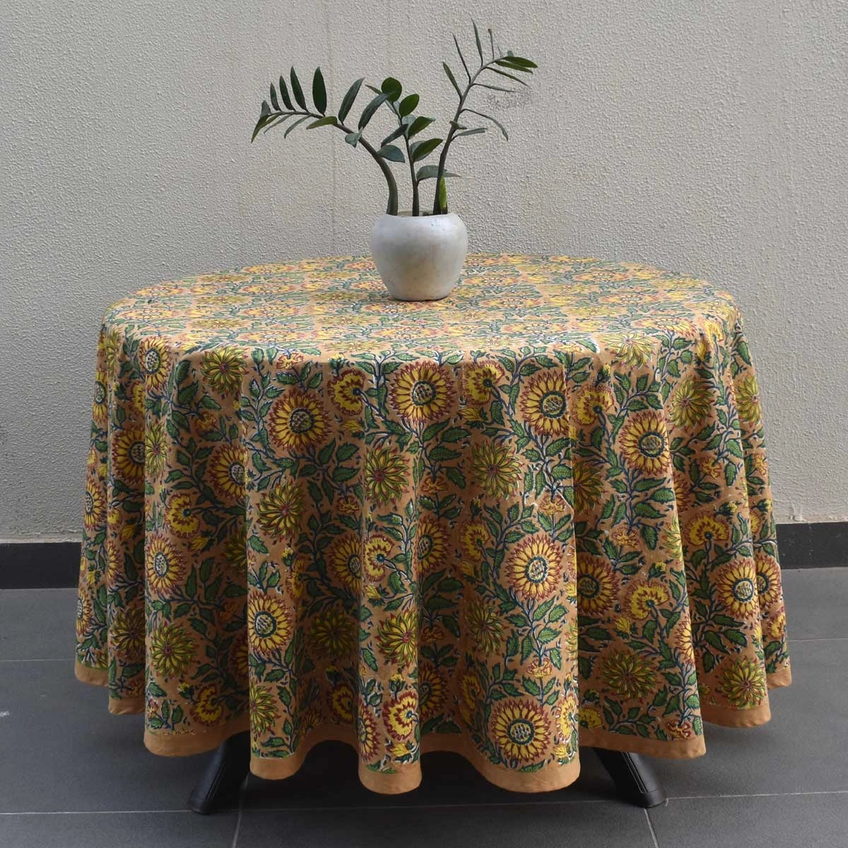 Round table with a floral patterned tablecloth against a gray wall.