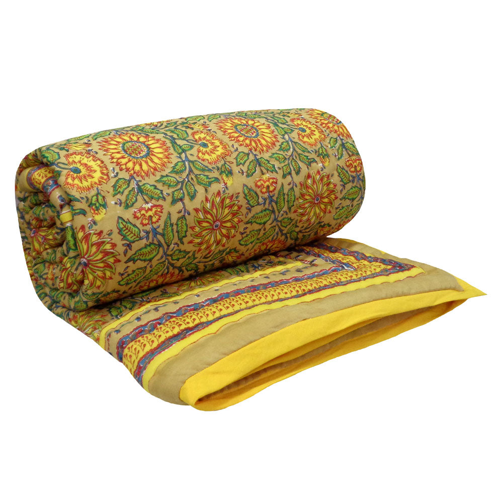 A rolled and folded patterned textile, likely a quilt, comforter, or throw, featuring a yellow and orange floral design with green leaves on a beige background, with a yellow border and purple decorative stripes.