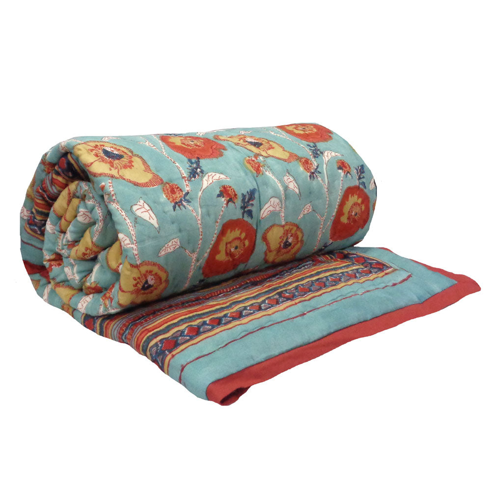 A rolled-up quilted blanket with a turquoise blue background, featuring a colorful floral pattern in orange, yellow, and red, with a striped border and a solid red edge.